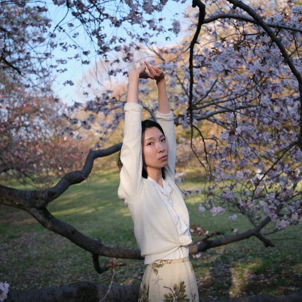 A woman stretching gracefully outdoors, surrounded by nature and soft light.